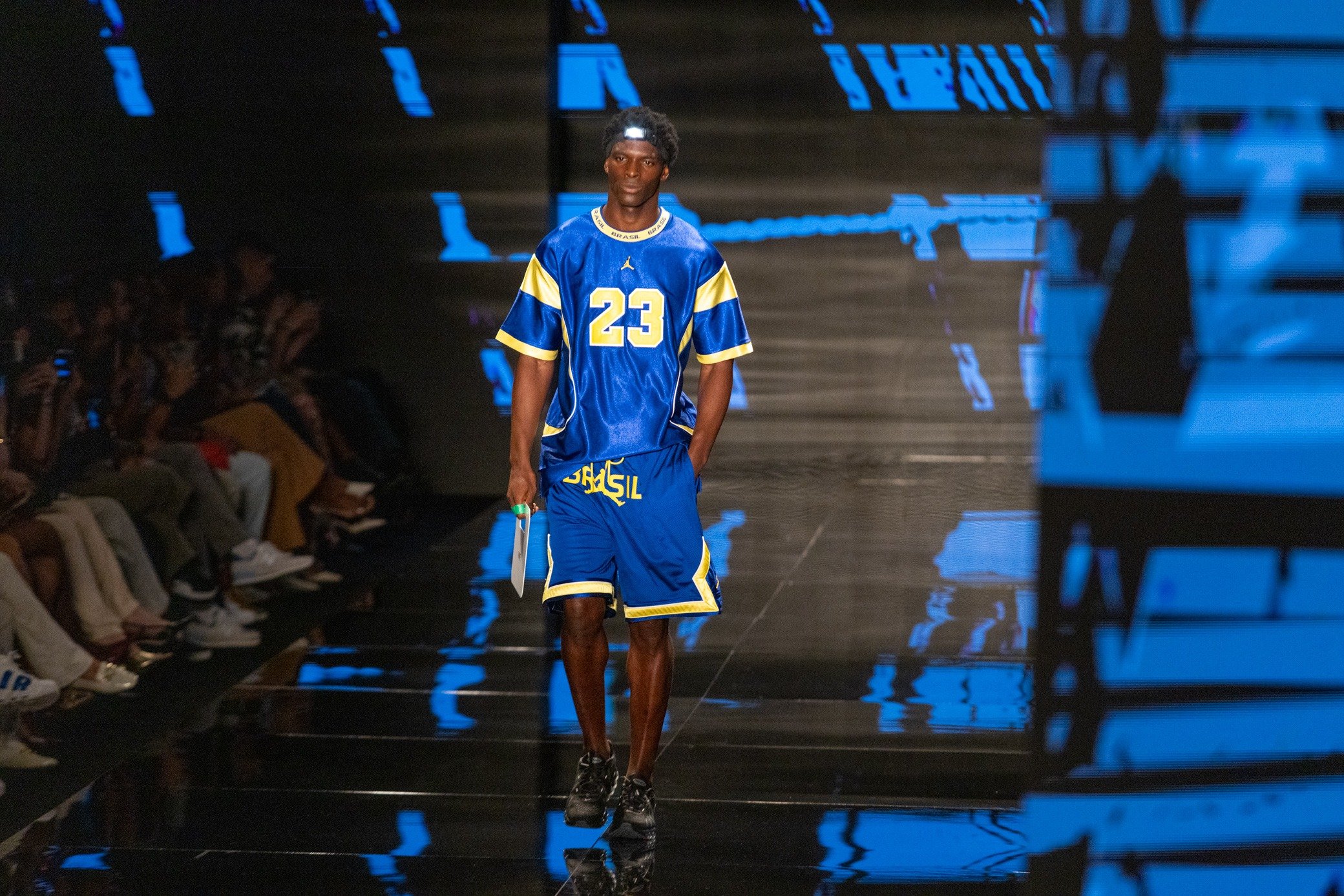 Moda inverno 2026: modelo desfila com conjunto esportivo azul e amarelo oversized na passarela, clima urbano.