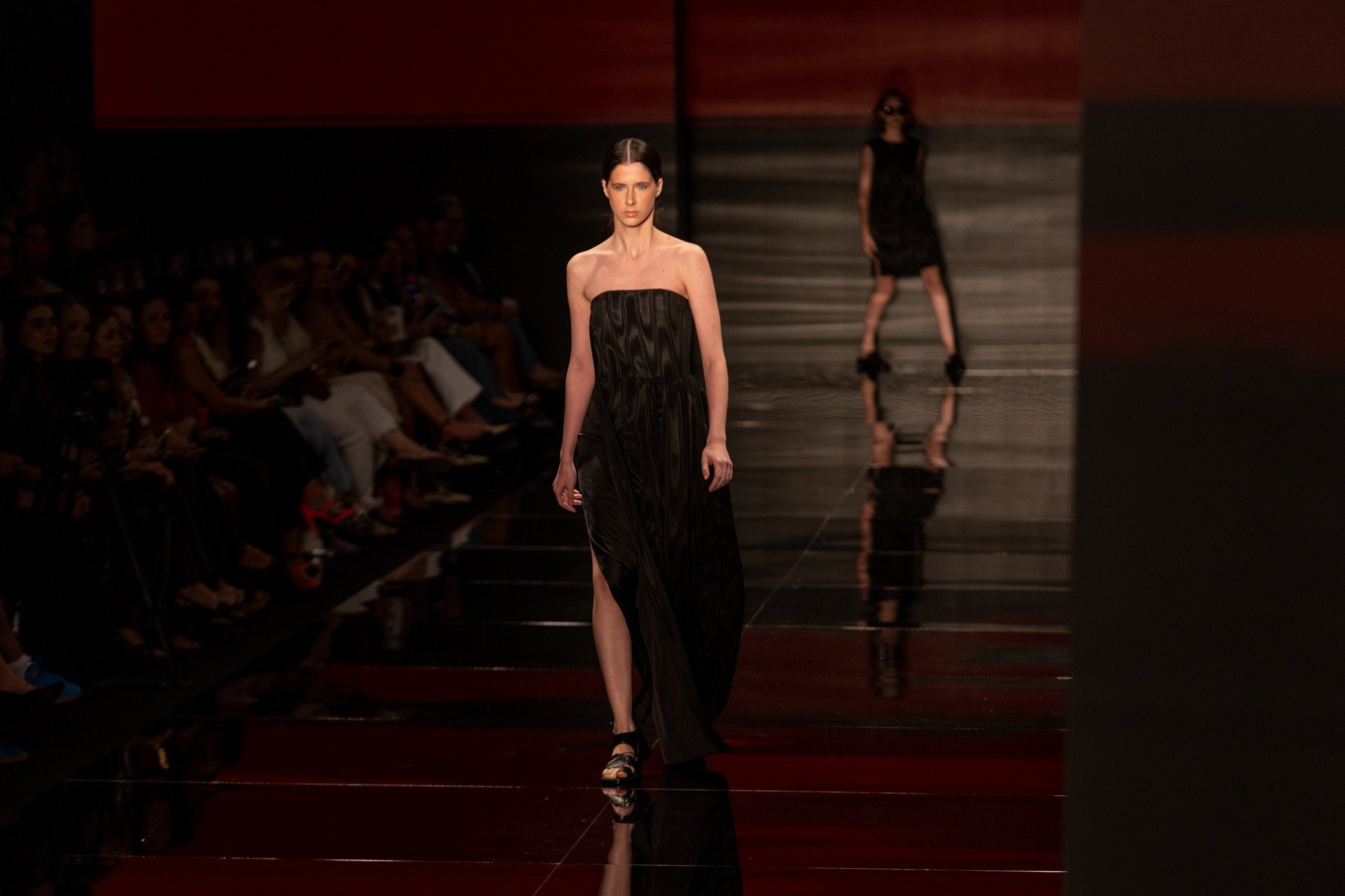 Moda inverno 2026: modelo desfila com vestido preto tomara que caia de brilho sutil em passarela escura e elegante