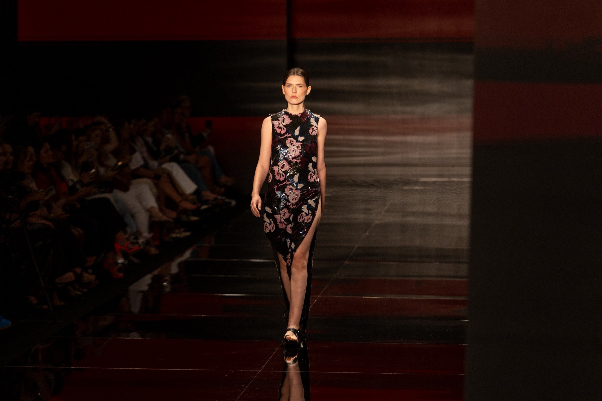Moda inverno 2026: modelo desfila vestido floral com brilho e fenda alta em passarela escura, clima sofisticado.