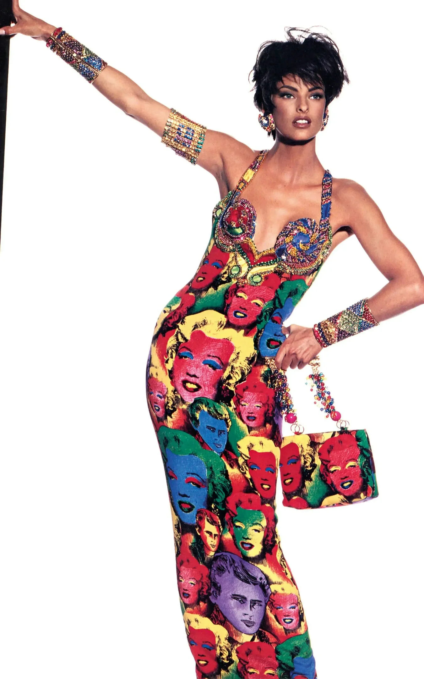 Modelo posa com vestido Versace justo e longo em estampa pop art multicolorida, combinando acessórios de pedrarias vibrantes