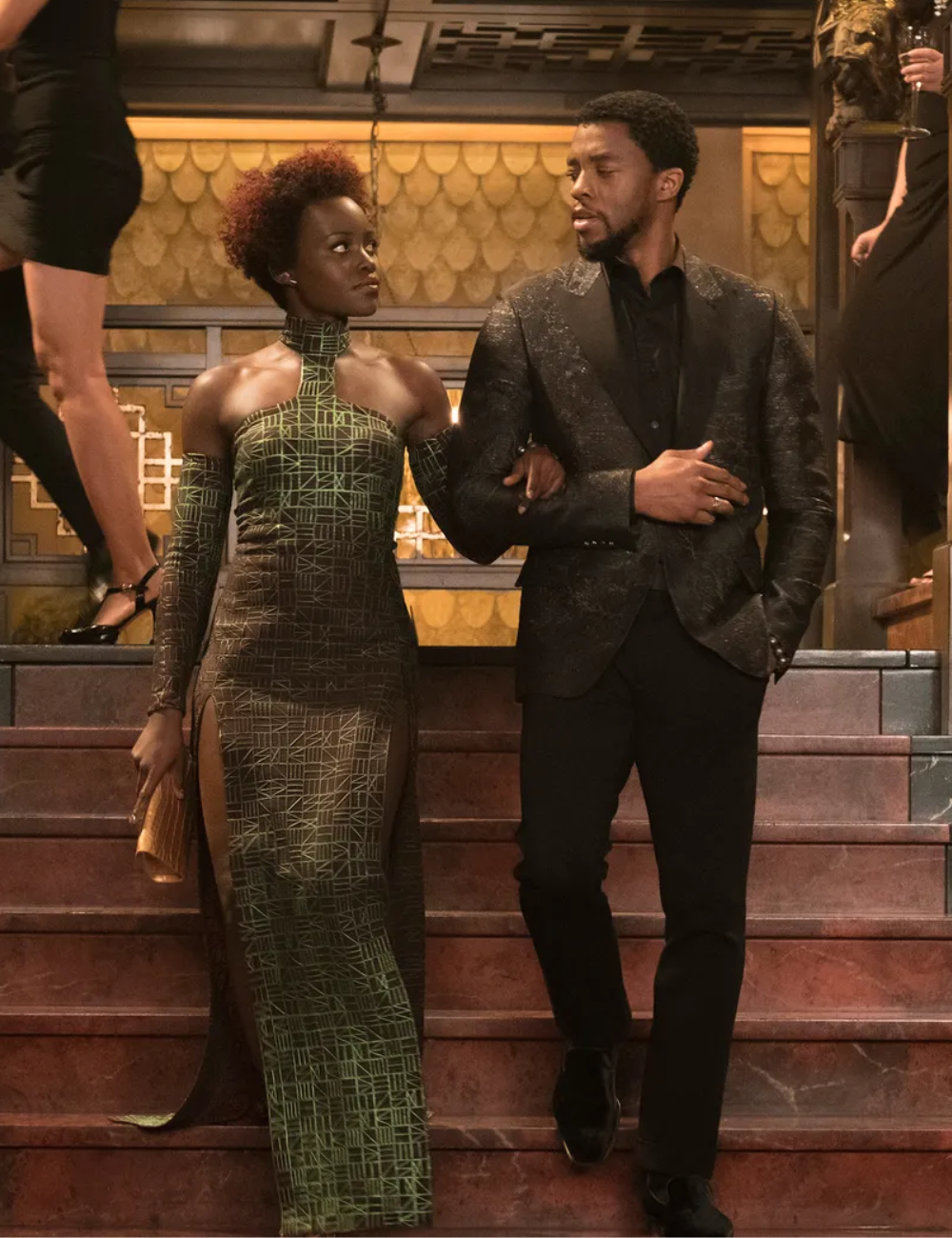 Ruth E. Carter cria look elegante com vestido verde geométrico de modelagem justa e fenda, e terno preto texturizado.