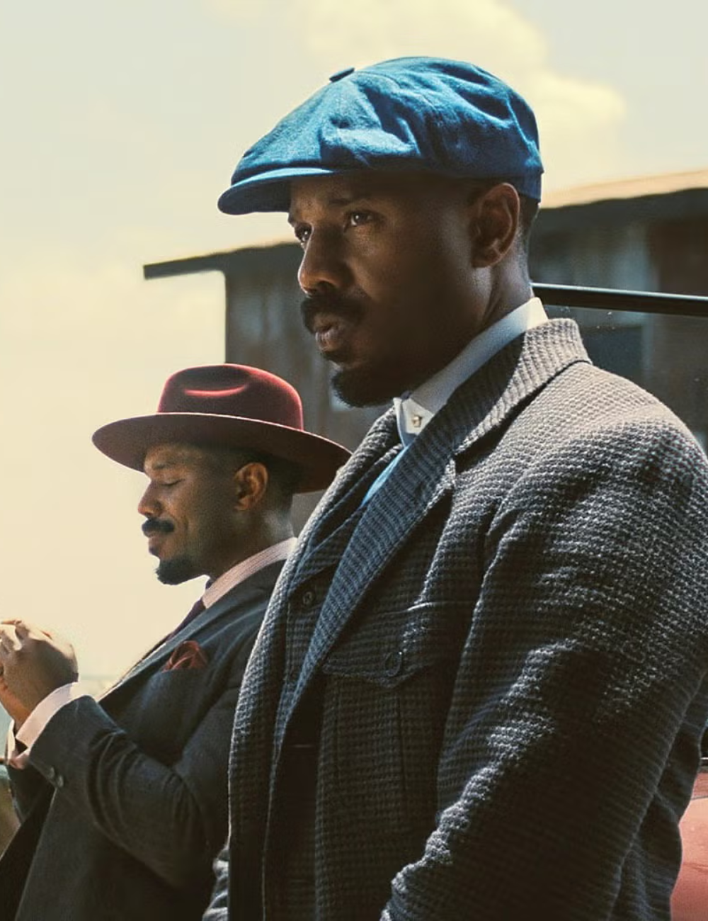 Dois homens vestem peças clássicas de lã e algodão em tons sóbrios, com boinas e chapéus estruturados.