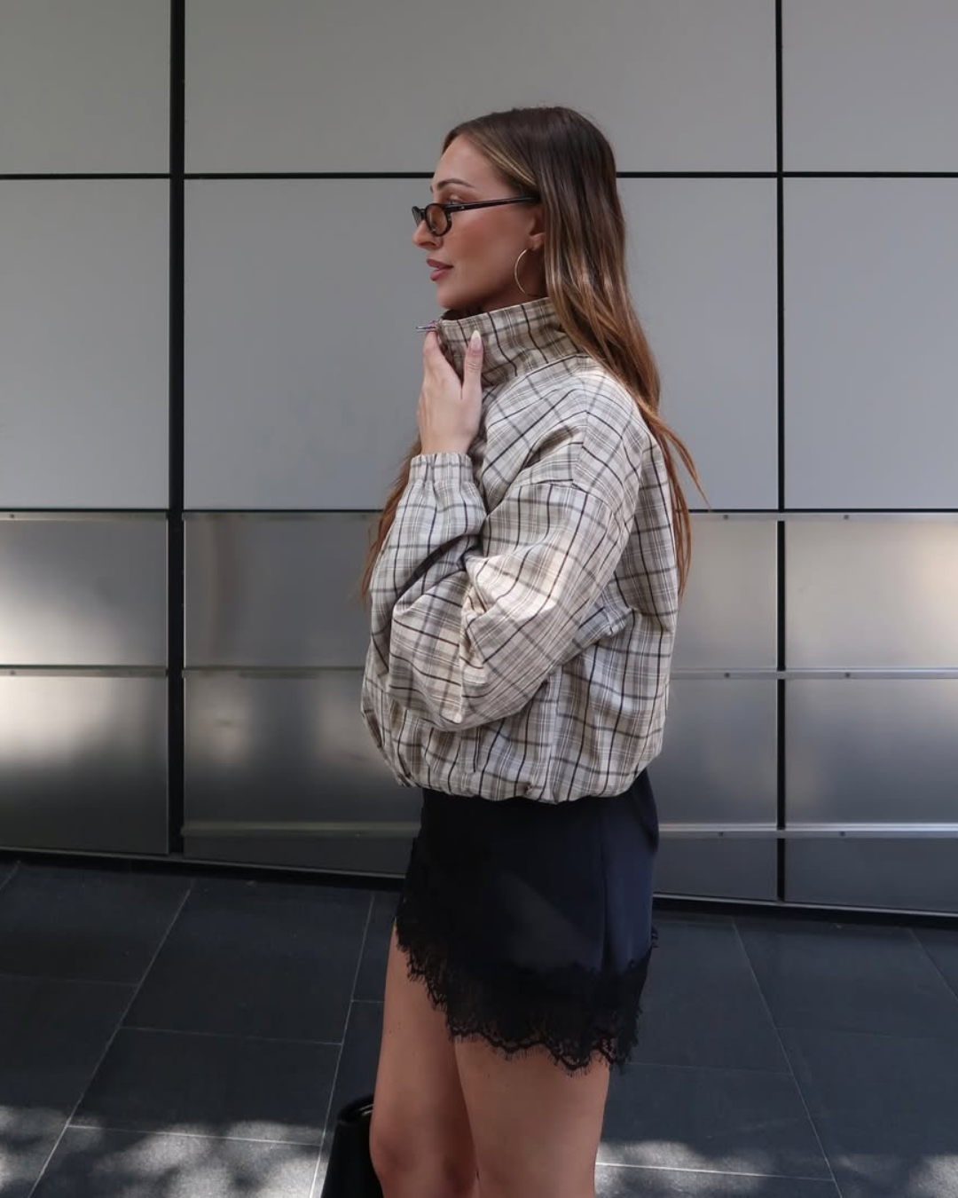 Sapatos confortáveis femininos compõem look urbano com camisa xadrez bege, short preto rendado e modelo posa elegante.