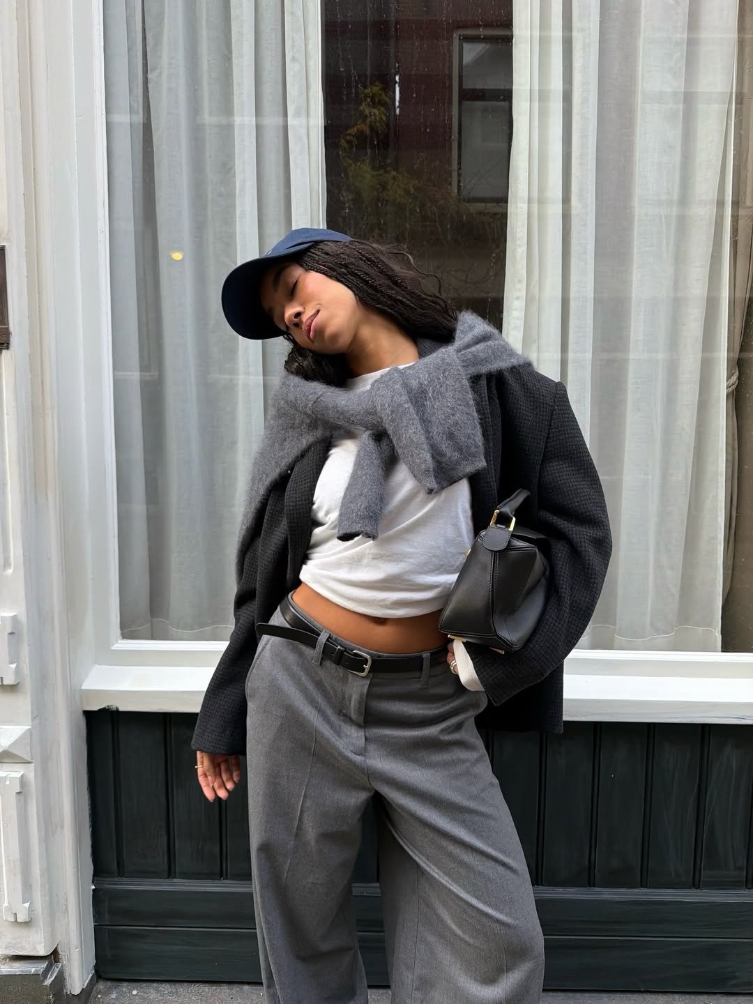 Modelo posa com look urbano em preto, branco e cinza, calça ampla, blazer e bolsa, com sapatos confortáveis femininos