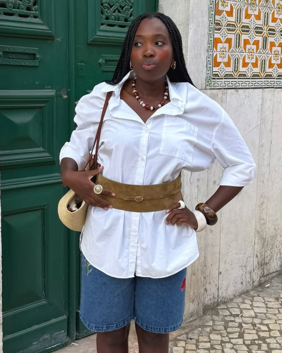 Modelo posa com camisa branca ampla, bermuda jeans e cinto marrom, look para sapatos confortáveis femininos