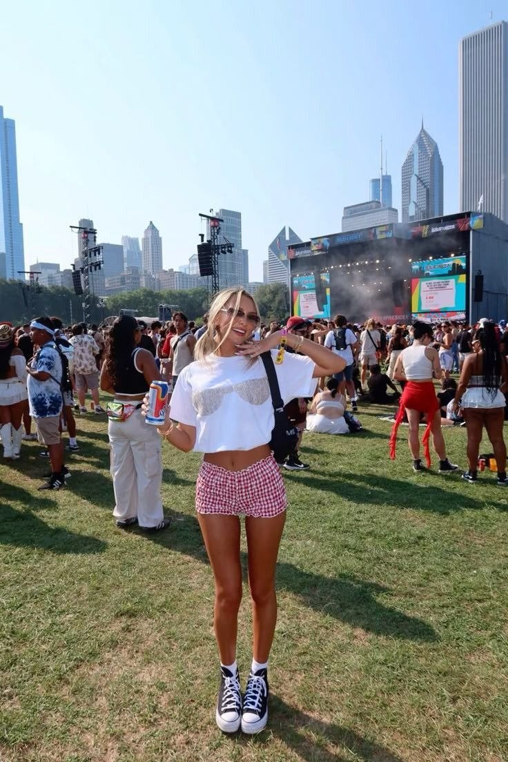 Melhores sapatos em look de festival: modelo posa com tênis preto, shorts xadrez rosa e camiseta branca, clima leve.