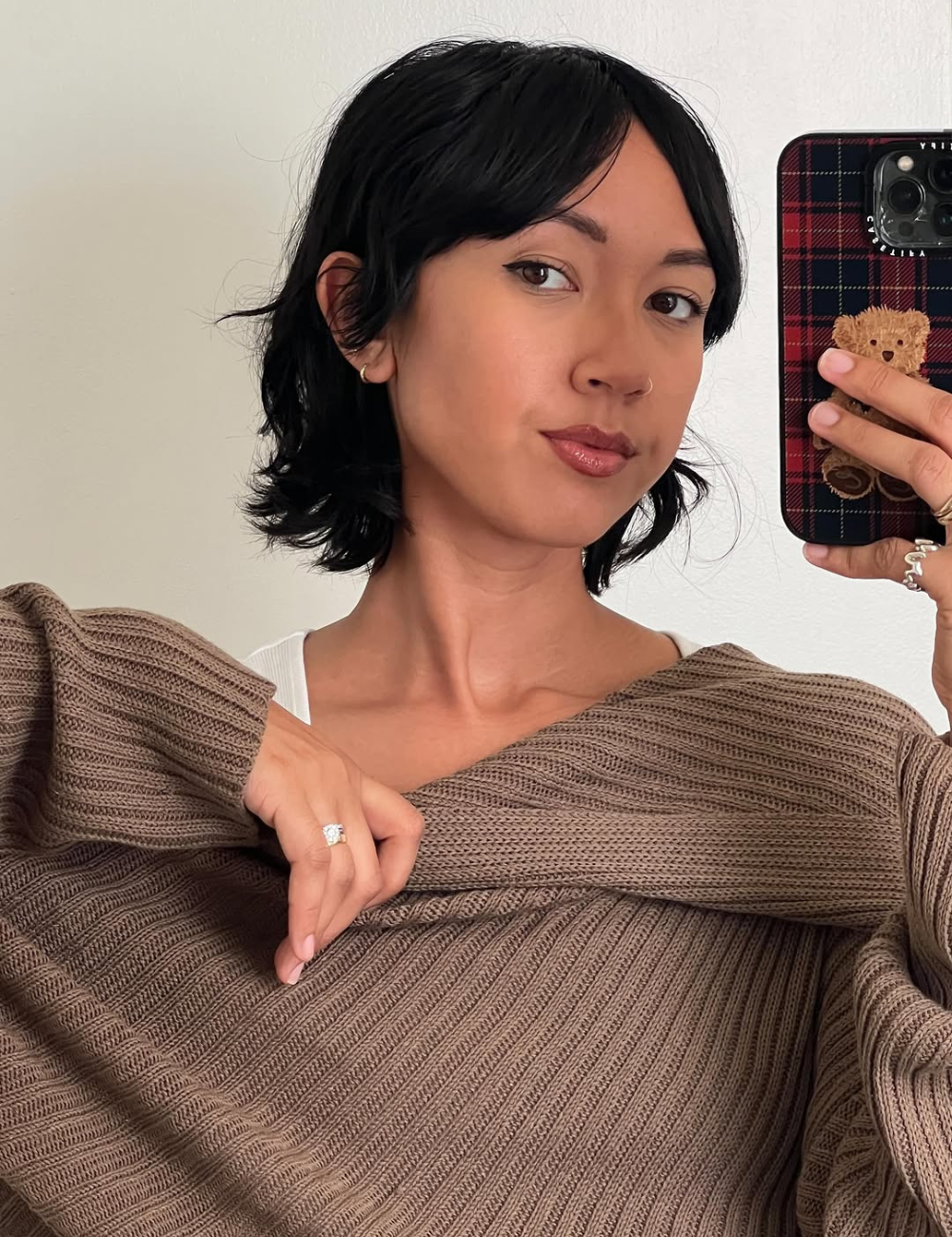 Modelo posa em selfie com corte curto preto, malha canelada marrom e clima leve, ideal para shampoos para cabelo fino.