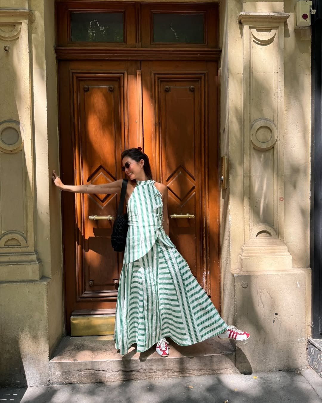 Looks para a copa: modelo posa com vestido listrado verde e branco, babados e tênis vermelho diante de porta clássica.