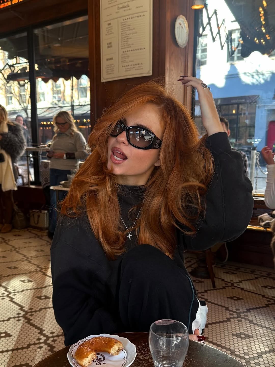 Opções de tinta para cabelo ruivo em destaque: modelo posa de moletom preto e óculos escuros em café acolhedor.