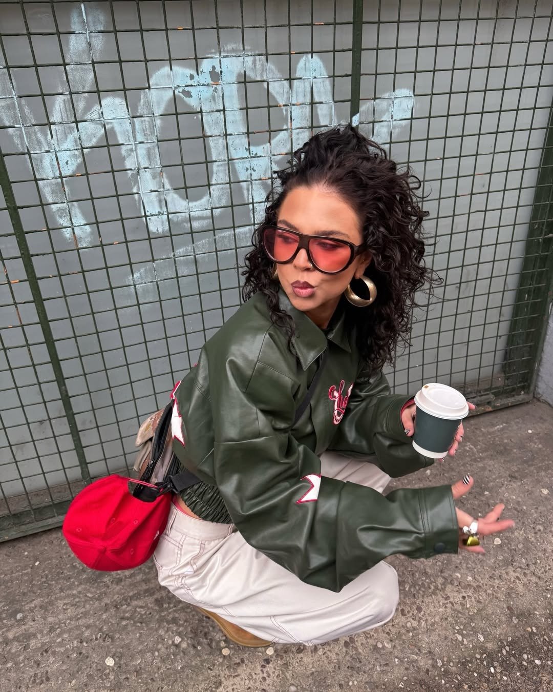 Modelo agacha com jaqueta verde de couro, calça off-white e cachos soltos; melhor shampoo para cabelos oleosos e finos.