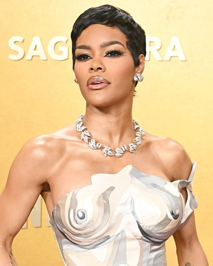 Modelo posa com halo lips brilhosos em tom nude, vestido tomara que caia com estampa abstrata em bege e cinza, joias