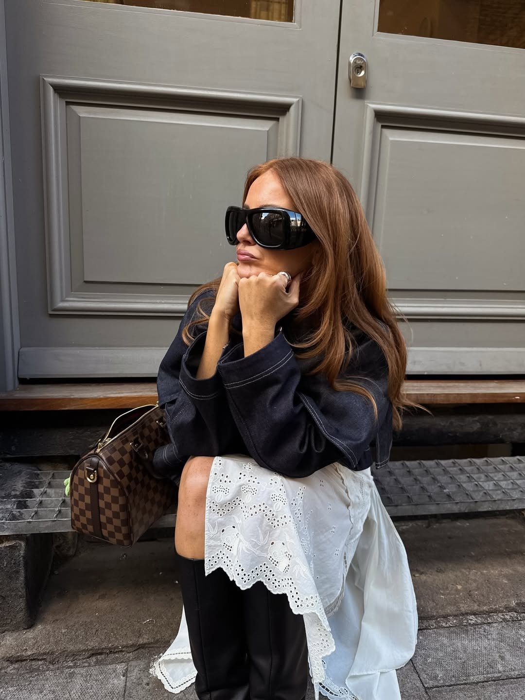 Modelo posa sentada com jaqueta escura, saia branca laise e botas pretas; melhor shampoo para cabelos oleosos e finos.