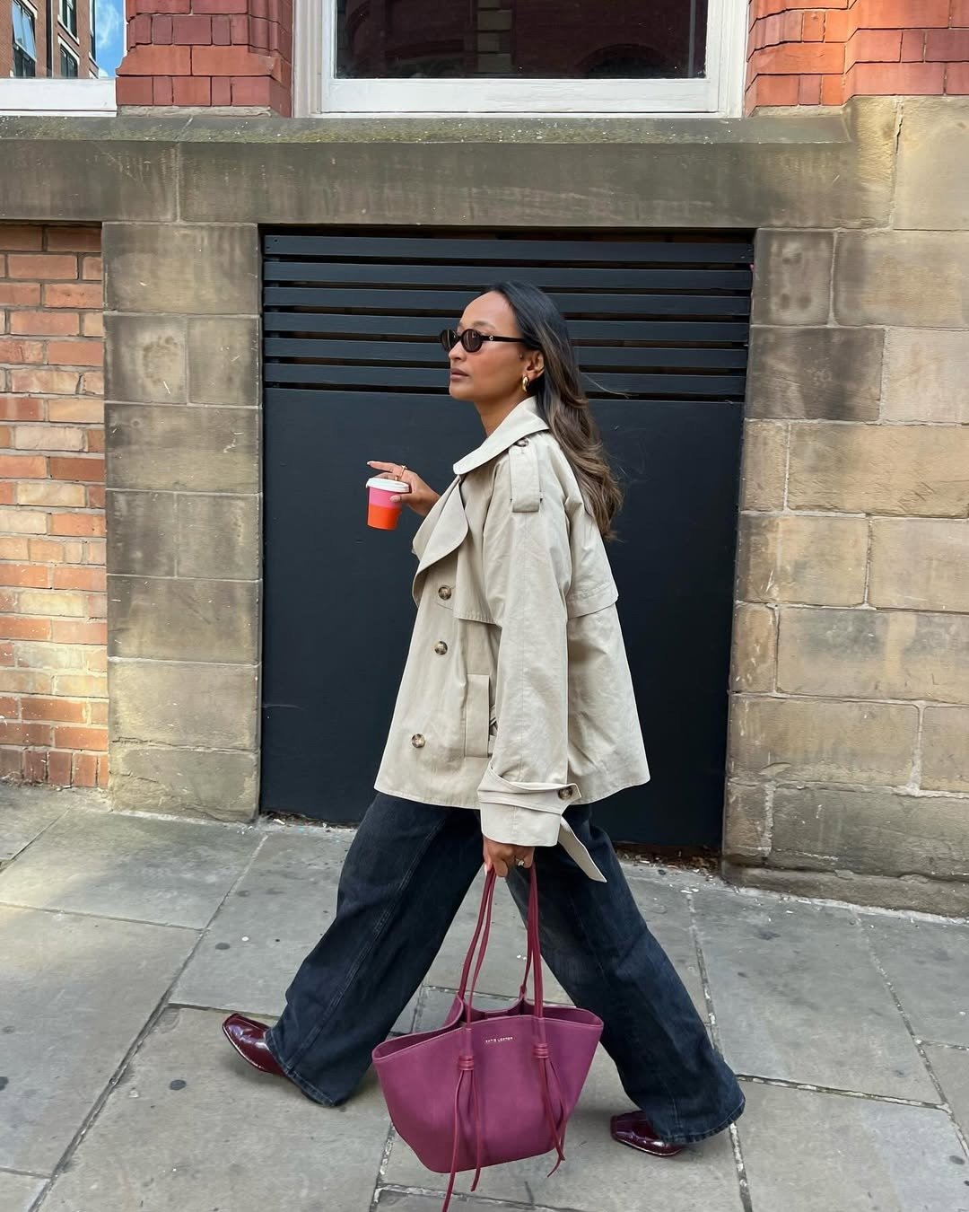 Looks de outono com modelo caminhando de trench bege, jeans amplo e bolsa vinho em rua urbana, clima elegante e sereno.