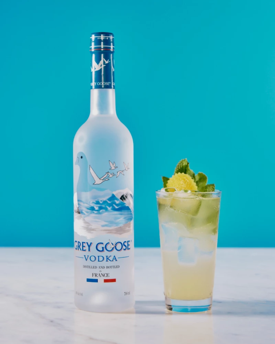 drinks com vodka fáceis Grey Goose ao lado de drink amarelo claro com gelo, hortelã e casca de limão