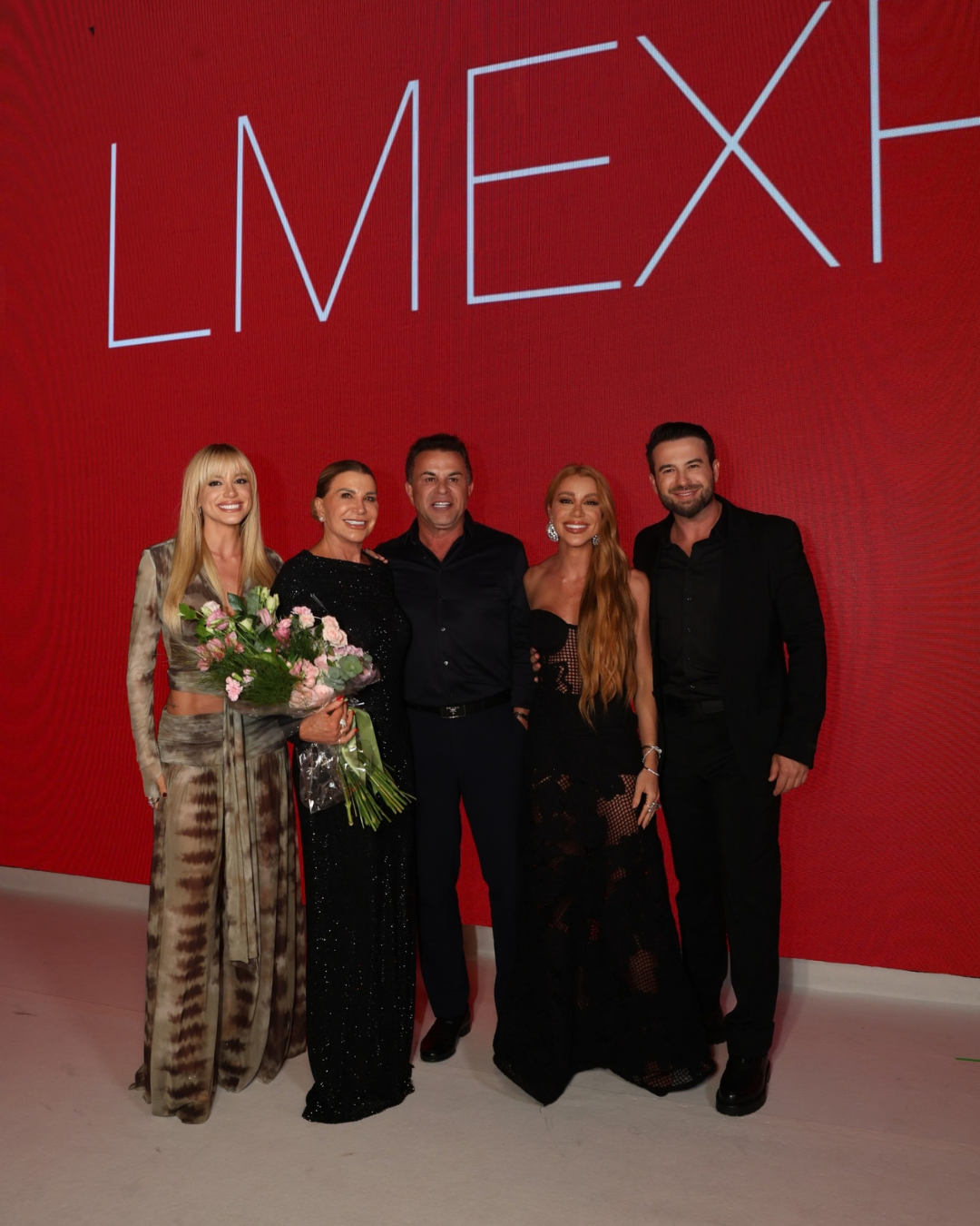 Tendências da primavera 2027 em looks de festa fluidos e pretos diante de painel vermelho