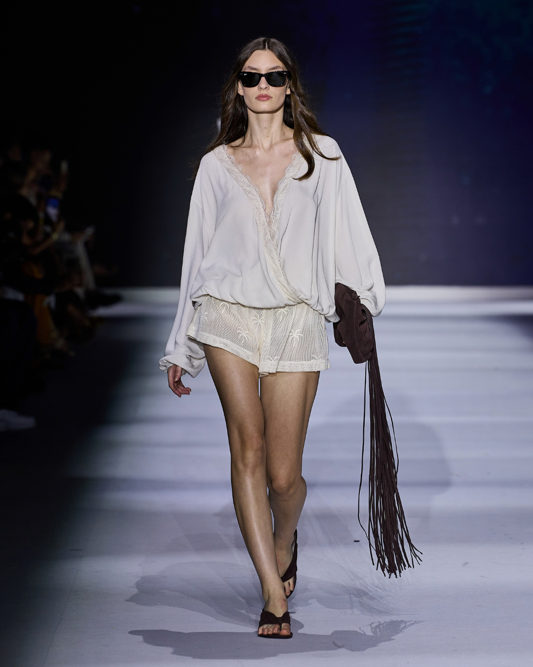 Modelo com blusa fluida off-white de renda, shorts de crochê bege e bolsa marrom de franjas, tendências de moda 2026