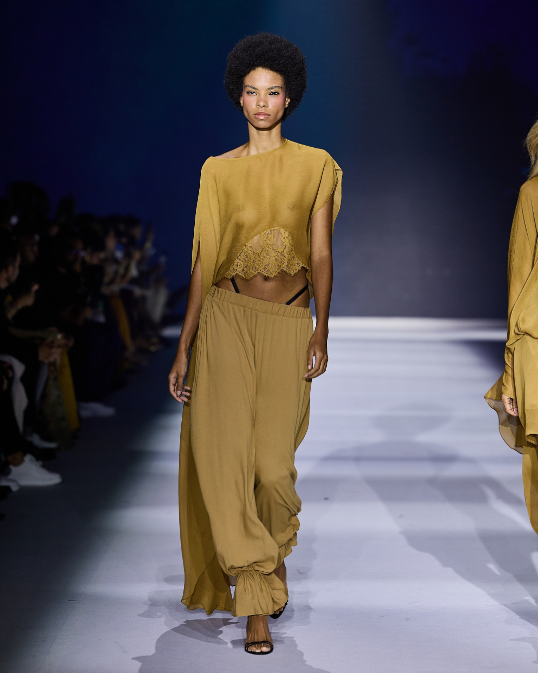 Modelo caminha com postura confiante usando top assimétrico com renda e calça ampla - tendências de moda 2026