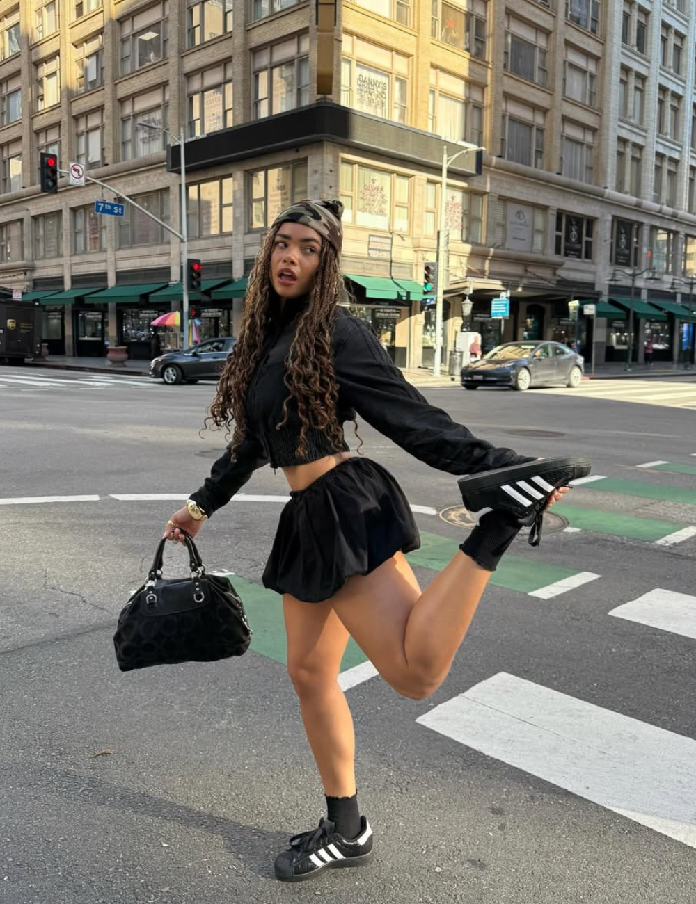 Modelo posa com tênis clássico estiloso preto e branco, look all black volumoso e atitude urbana em cruzamento.