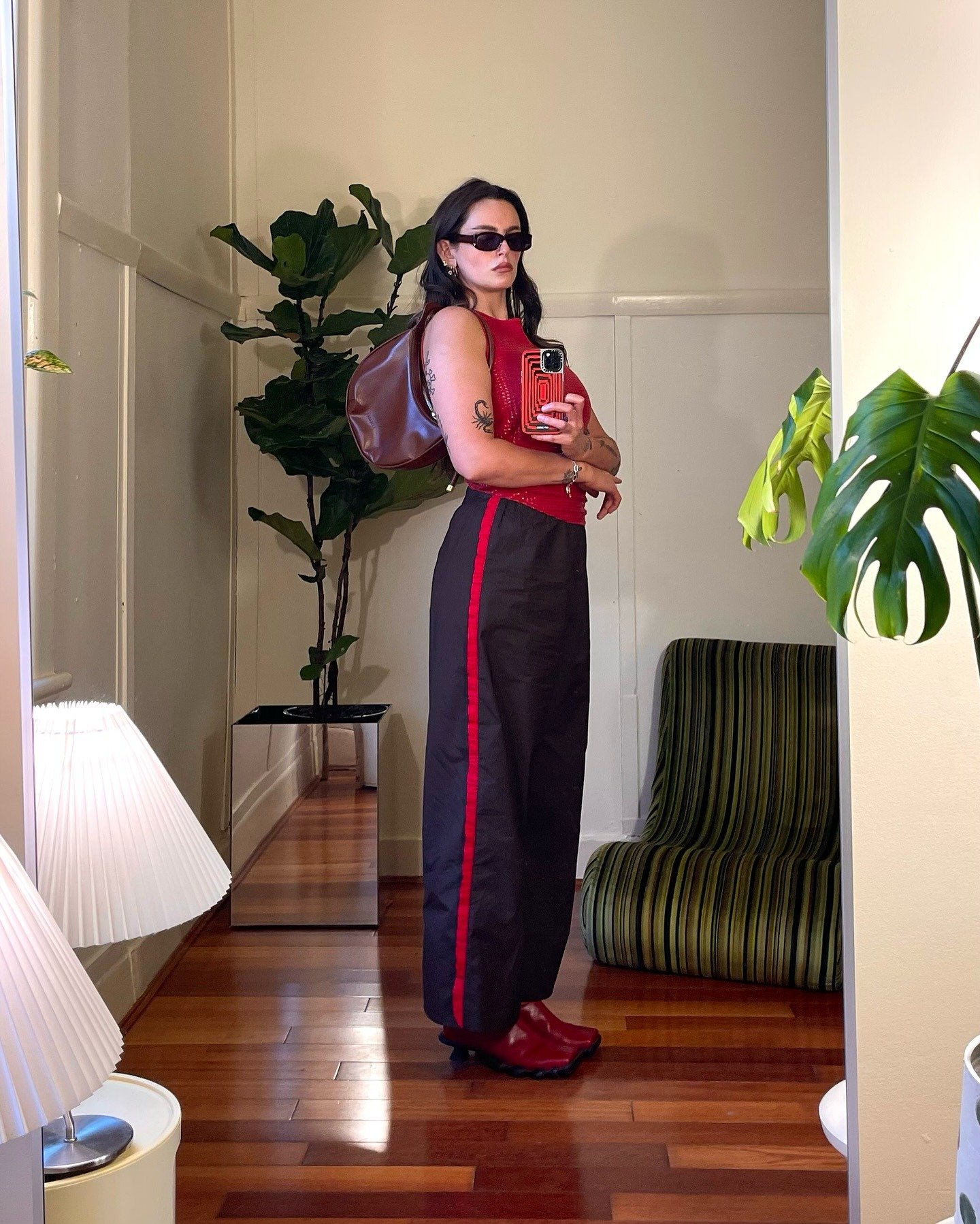 Looks da semana: modelo posa com regata vermelha, calça preta ampla e botas vermelhas em clima urbano sofisticado