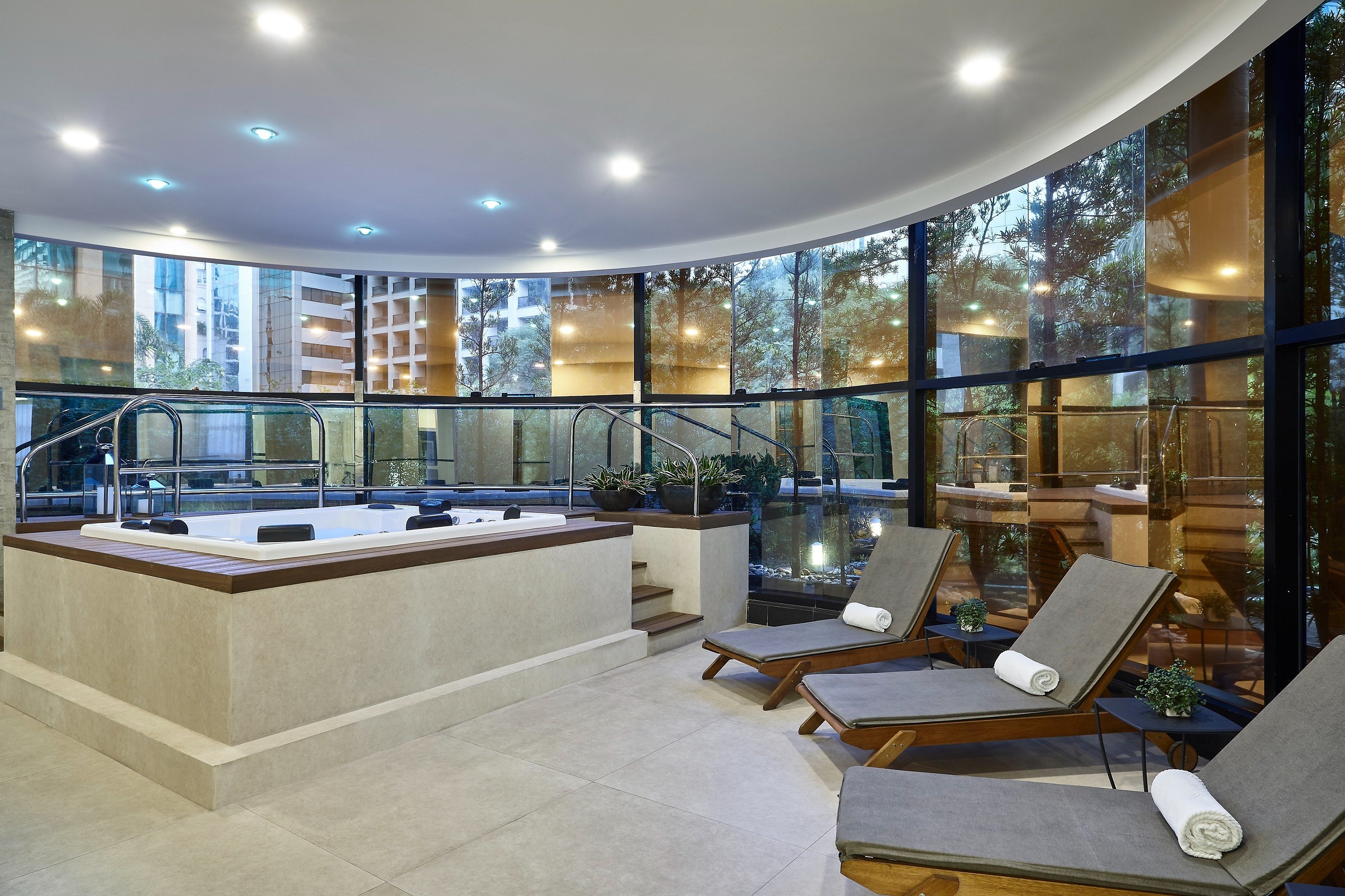 Sala de massagem com parede cinza escuro, mesa com toalha branca e manta cinza, banheira de madeira e iluminação suave com