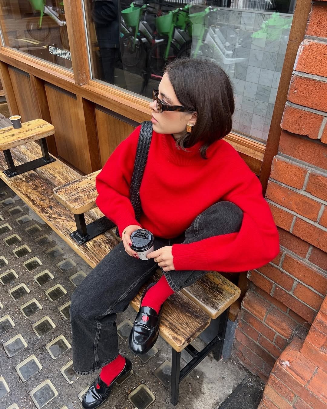 Modelo posa sentada com mocassim feminino com calça jeans grafite, tricô vermelho e clima urbano elegante;