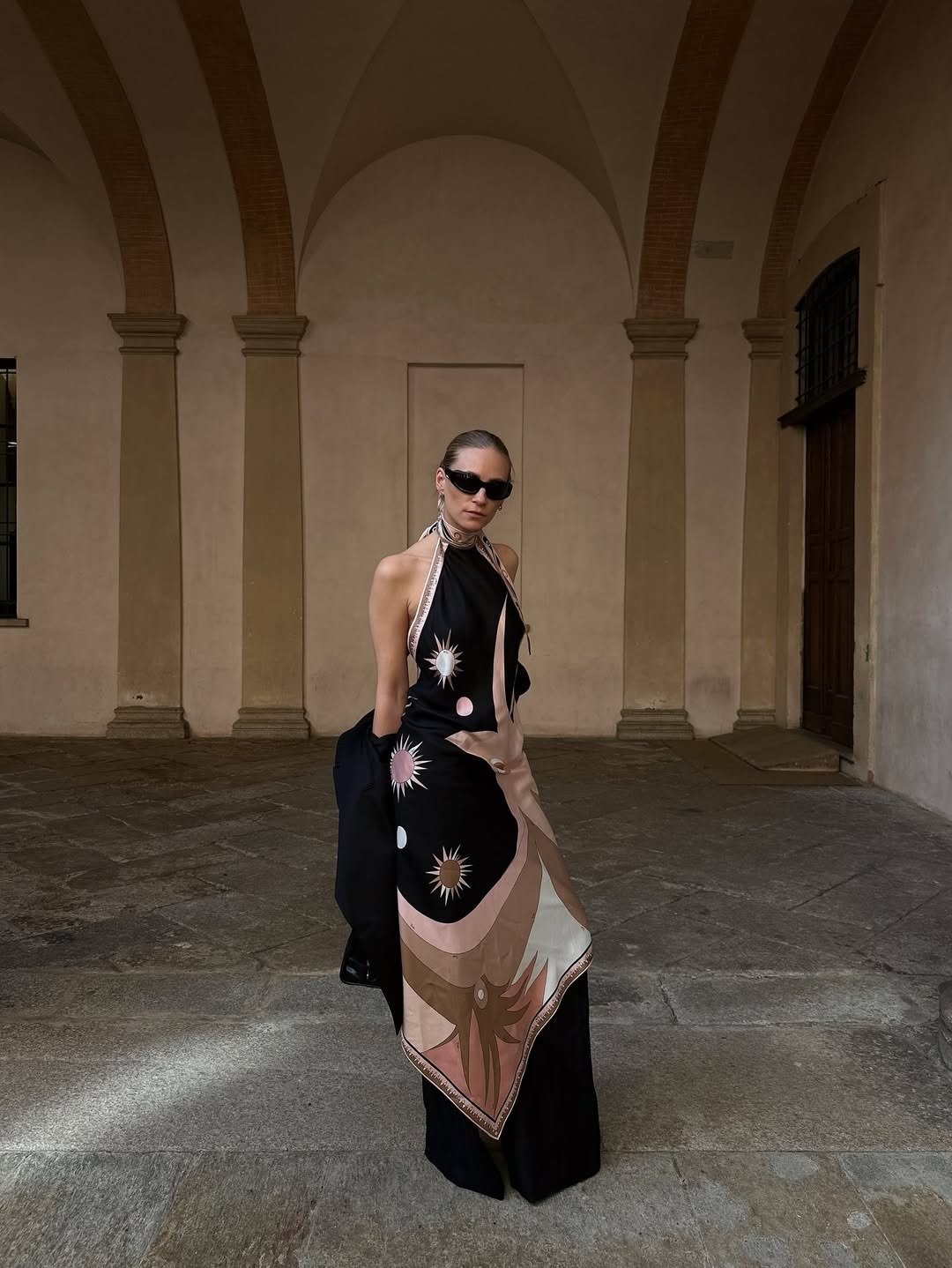 Modelo posa com vestido tendência 2026 em seda preta com estampas solares em tons terrosos e rosa, estilo fluido e