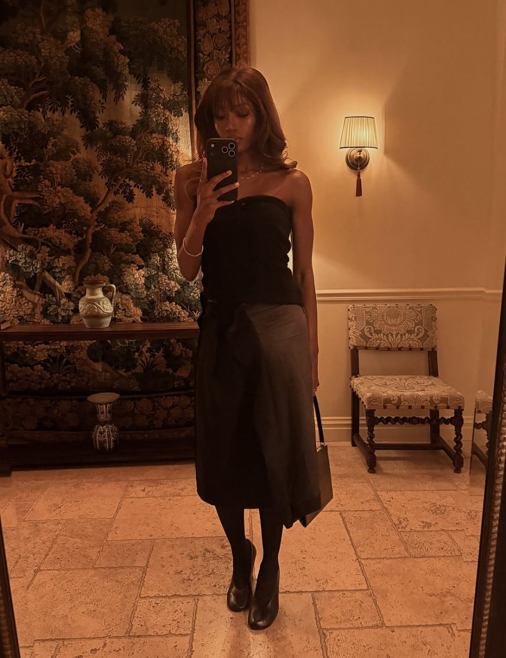 Modelo posa em ambiente sofisticado com vestido preto midi, bolsa estruturada e vamp pumps de couro preto.