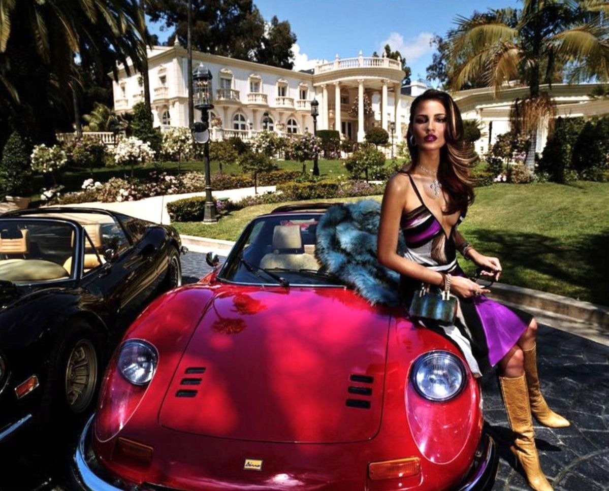 Modelo posa com vestido Versace em seda colorida com decote profundo, botas de couro caramelo e bolsa estruturada, em clima