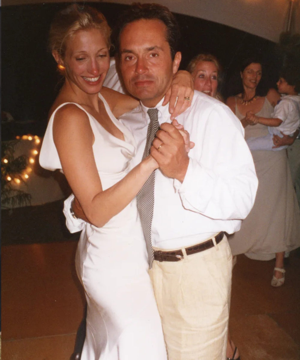 Carolyn Bessette veste vestido de casamento de cetim branco, com decote em V e caimento minimalista, em momento íntimo ao