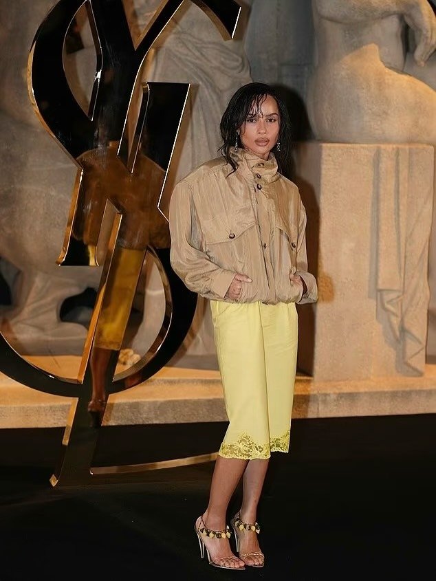 Modelo posa com jaqueta bege oversized de tecido leve e bermuda amarela com barra rendada, combinando elegância e conforto