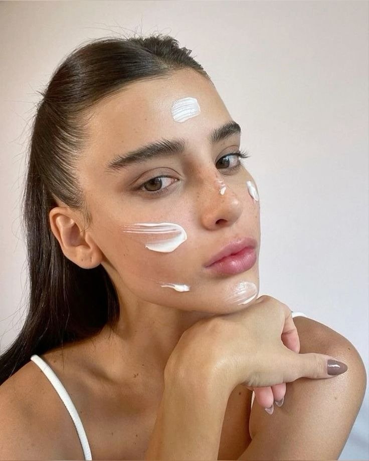 Melhor sabonete para o rosto em clima clean: modelo posa de regata branca com creme no rosto e fundo neutro.