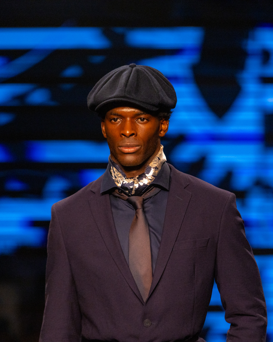 Acessórios tendência do inverno 2026: modelo posa com boina azul e lenço acetinado, em alfaiataria sóbria e elegante.