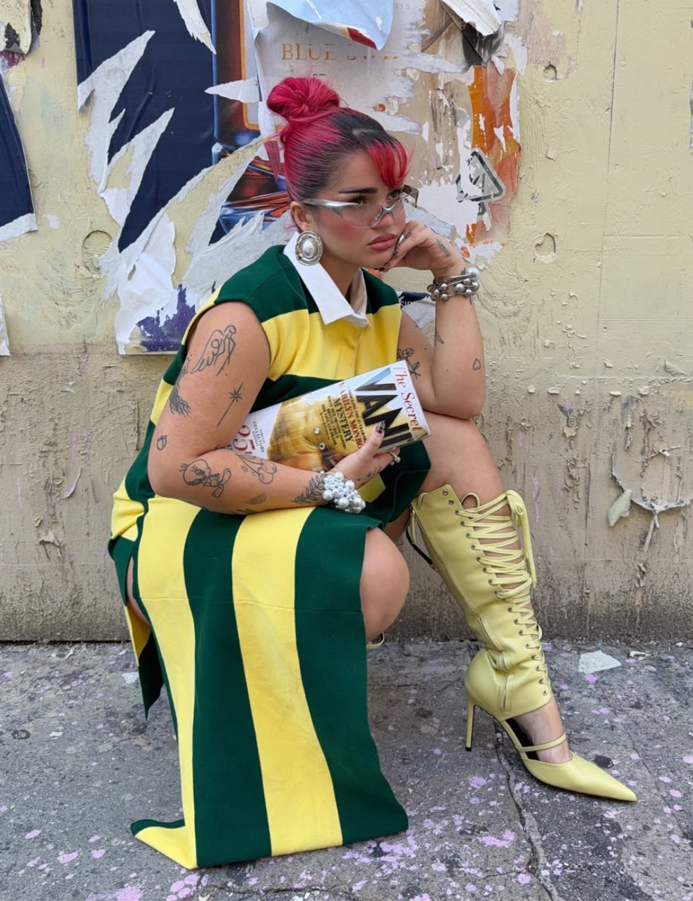 Modelo posa com armações estilosas para óculos de grau, vestido listrado verde e amarelo e bota de salto em clima ousado.