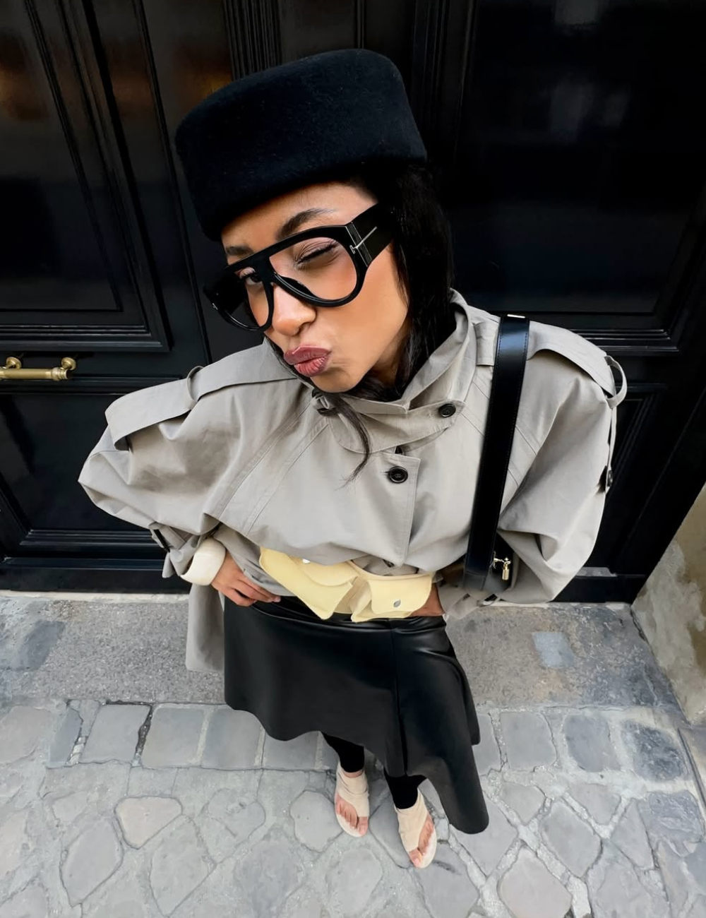 Modelo posa com armações estilosas para óculos de grau, trench bege e saia preta em clima urbano ousado.