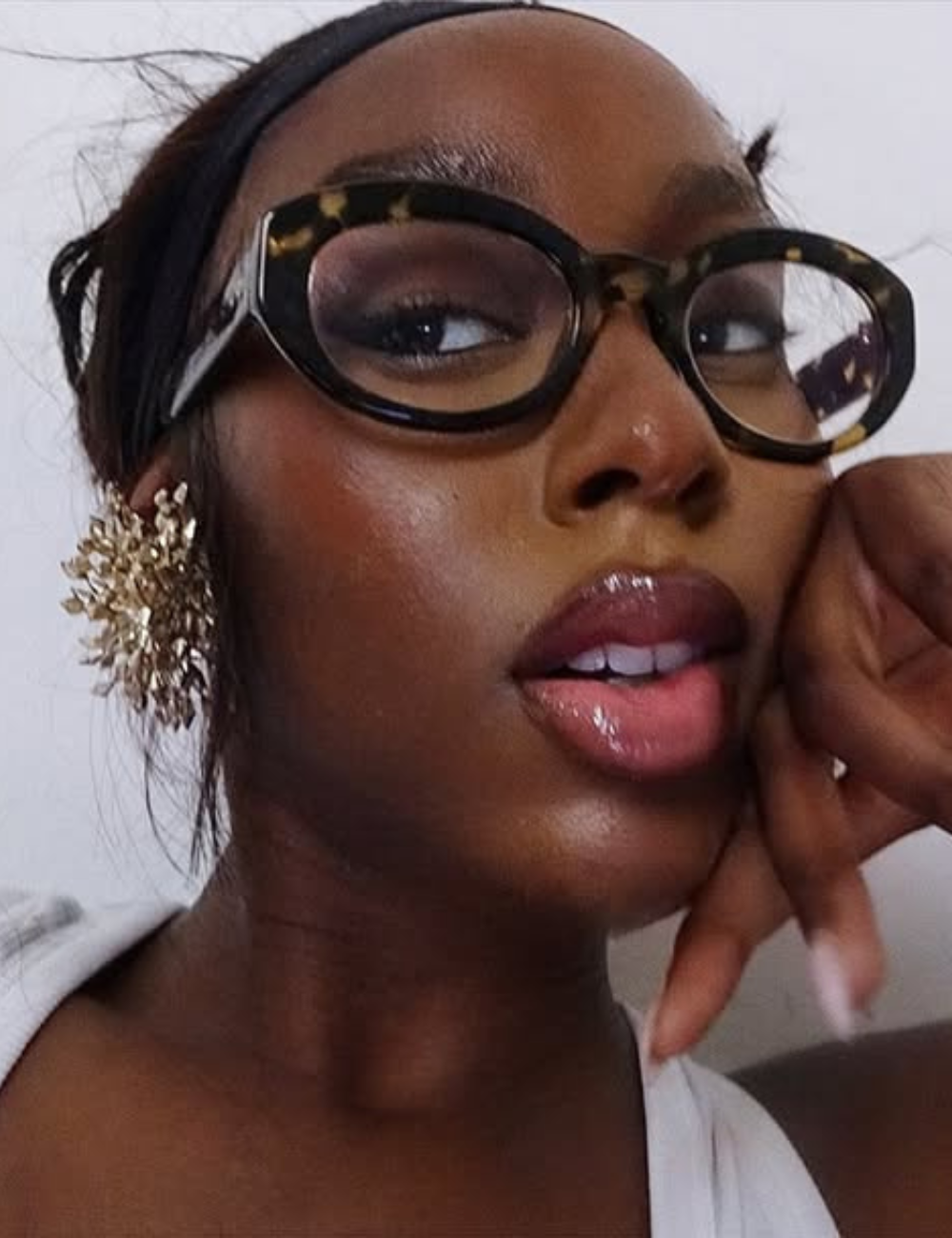 Modelo posa com armações estilosas para óculos de grau tartaruga, brinco dourado floral e beleza sofisticada.