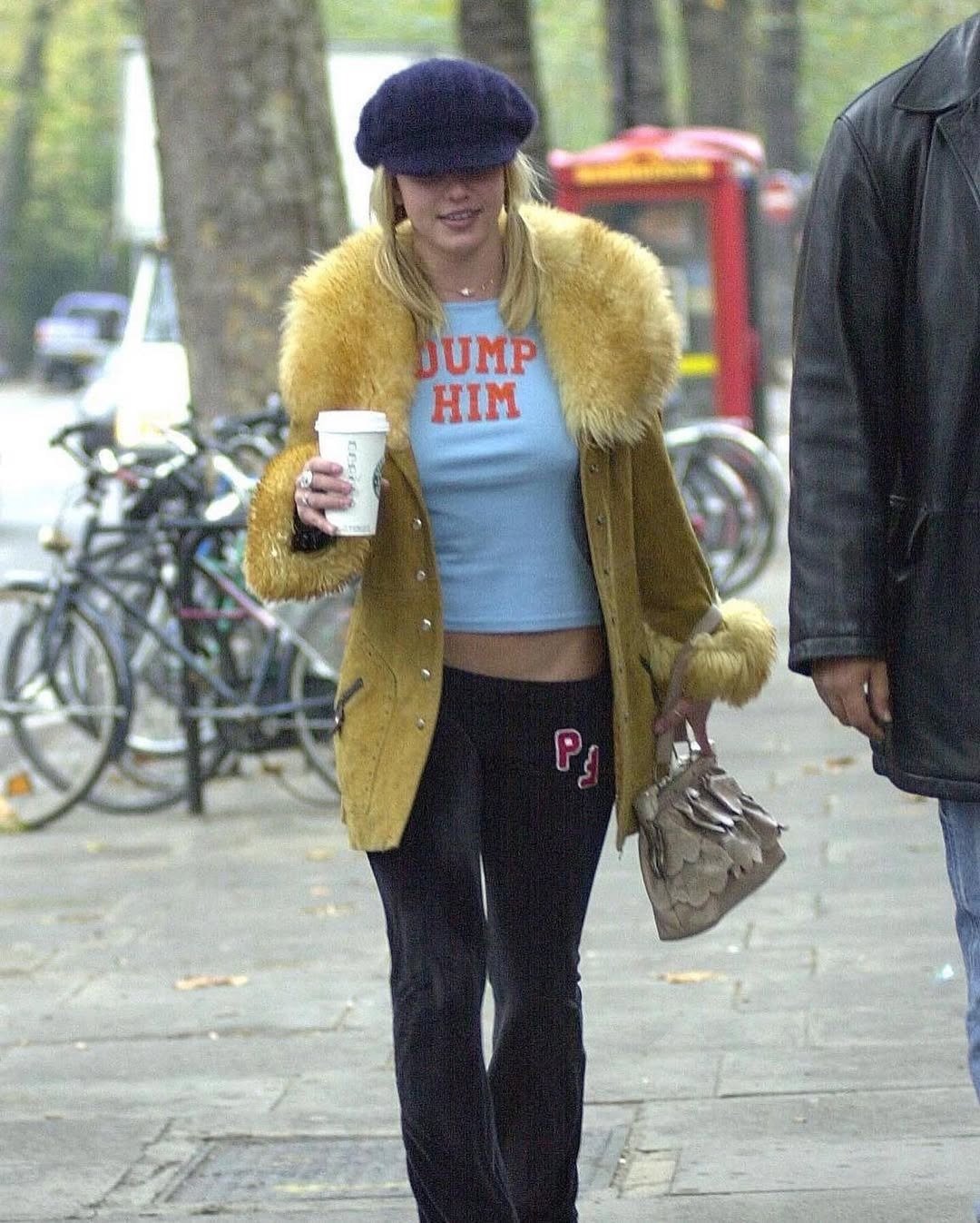 Modelo caminha com camiseta azul cropped, casaco felpudo mostarda e boina; clima casual. Texto: DUMP HIM