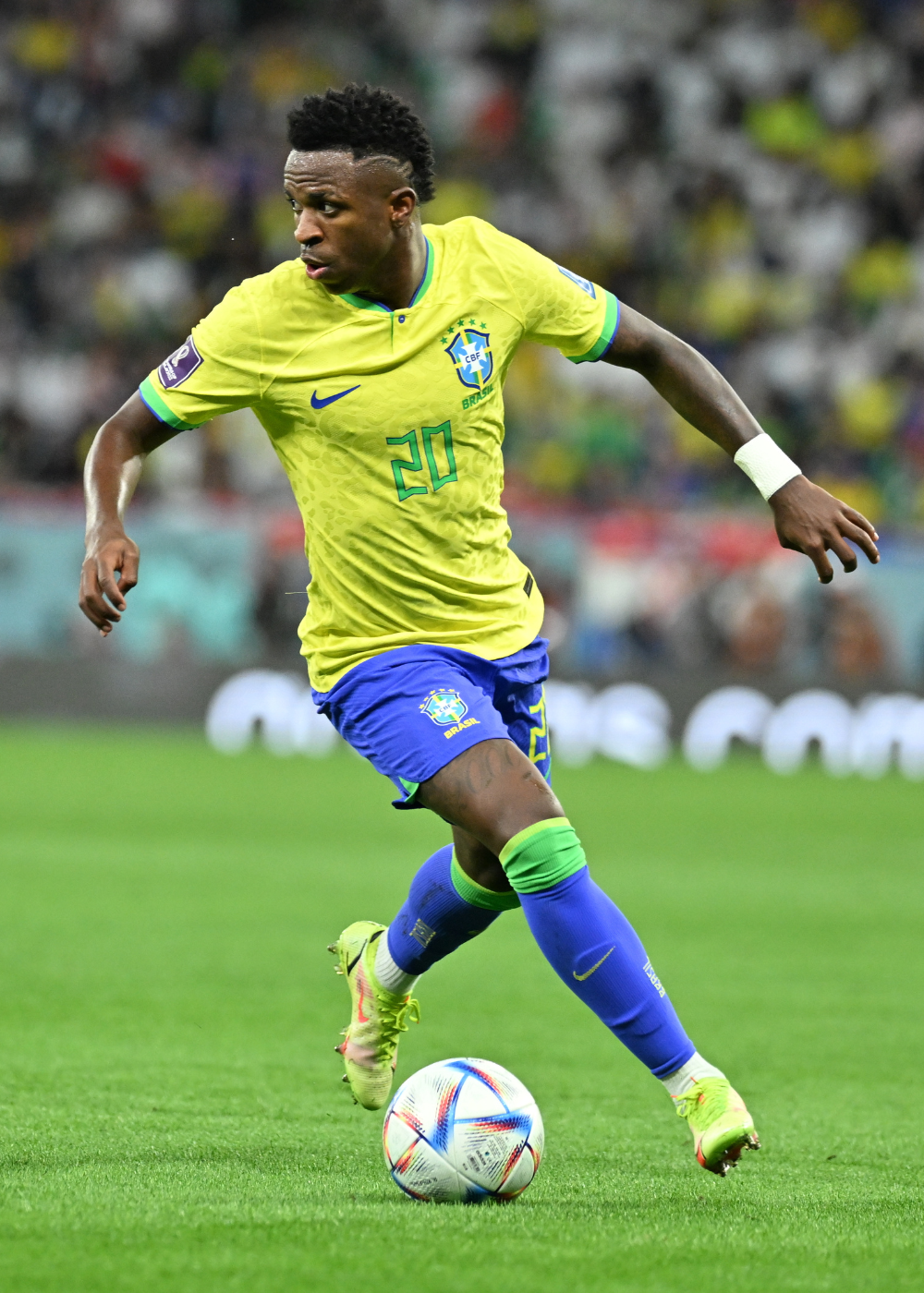 Jogador conduz a bola com camisas do Brasil amarelas texturizadas, short azul e energia competitiva no gramado.