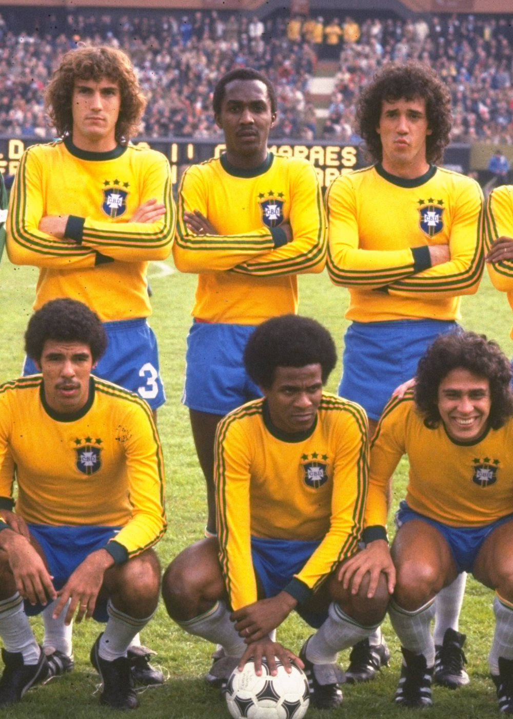 Jogadores posam com camisas do Brasil amarelas de manga longa, listras verdes e shorts azuis em clima clássico no estádio.