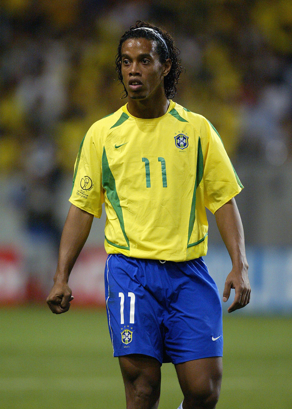 Modelo posa em campo com camisas do Brasil amarelas e recortes verdes, short azul e expressão focada.