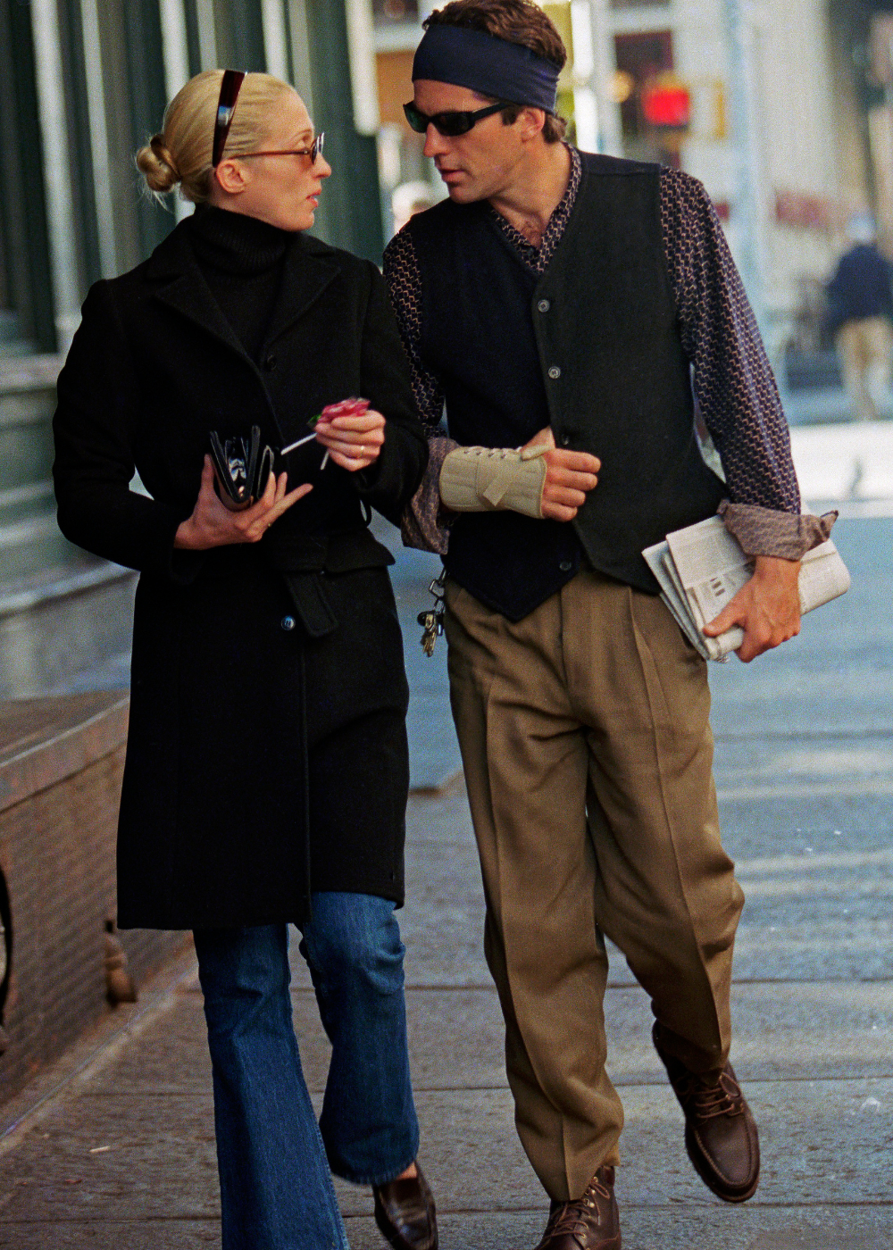 Estamos todos gostando das mesmas coisas: casal caminha e conversa com alfaiataria escura, jeans e tons neutros urbanos.