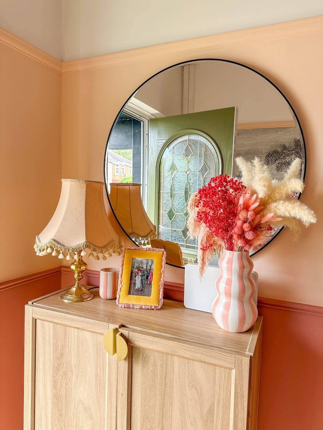 Como escolher cores para parede com pêssego e terracota em hall acolhedor, madeira clara, espelho redondo e flores secas