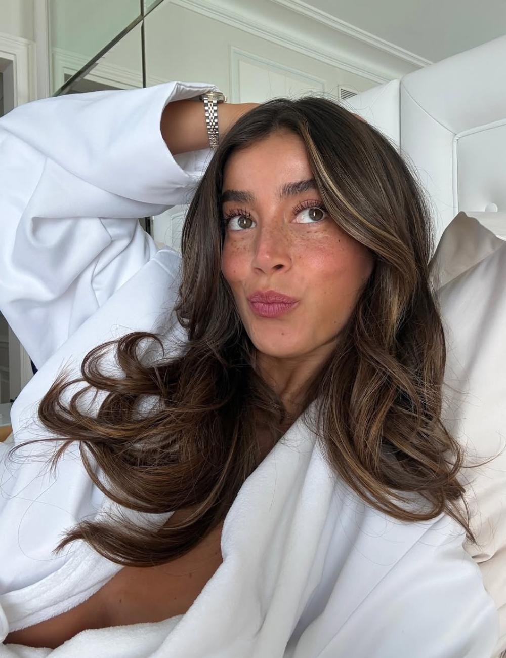 Como acabar com frizz no cabelo liso: mulher posa de roupão branco com fios castanhos polidos e clima leve.