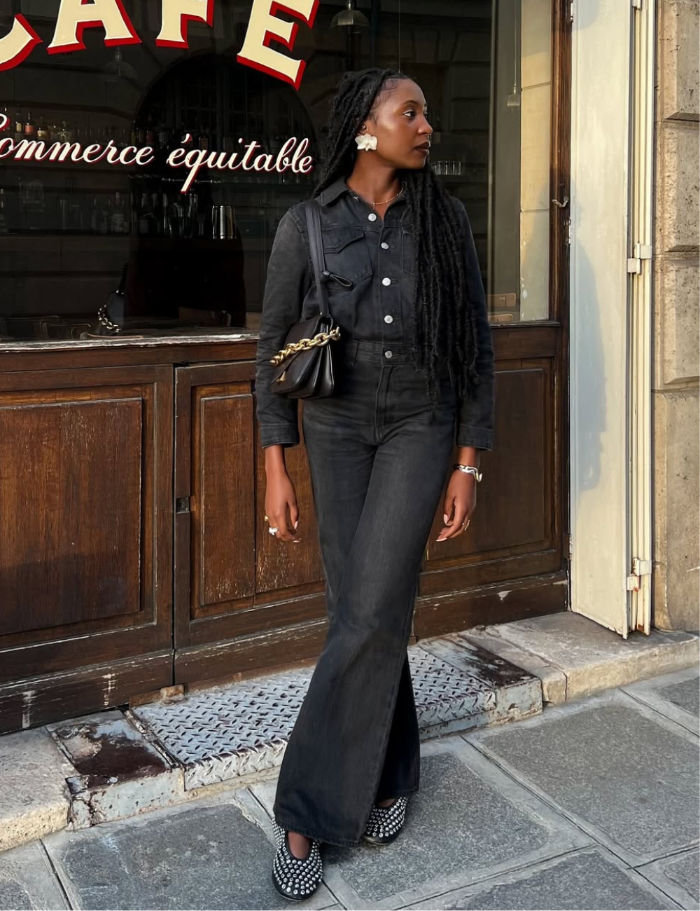 Modelo posa em look all black com jaqueta e calça flare jeans, bolsa de corrente dourada.