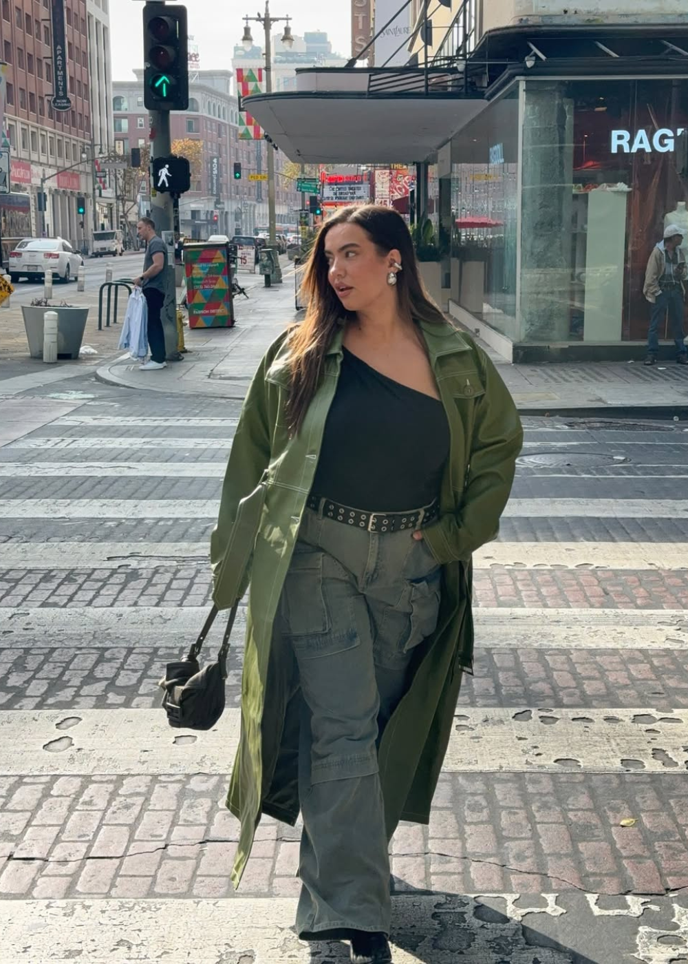 Looks de inverno 2026 com modelo posa em sobretudo verde, blusa preta assimétrica e cargo cinza em rua urbana.