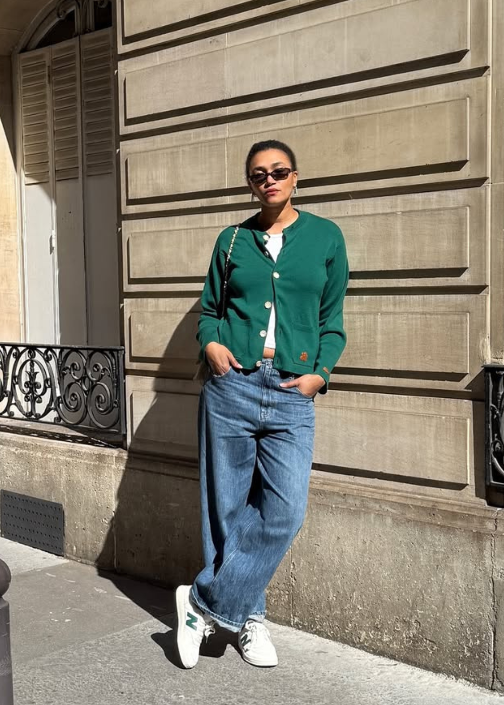 Looks de inverno 2026: modelo posa com cardigan verde, jeans amplo e tênis branco sob luz urbana elegante.