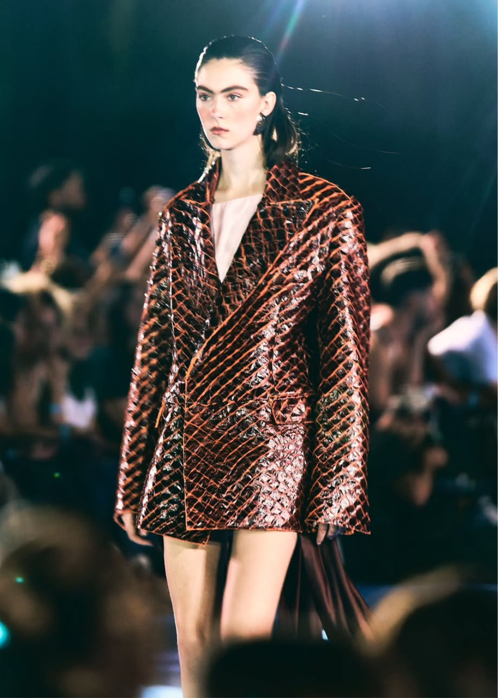 Desfile da MISCI na Sapucaí: modelo caminha com blazer vinho texturizado e brilho molhado sob luz dramática.