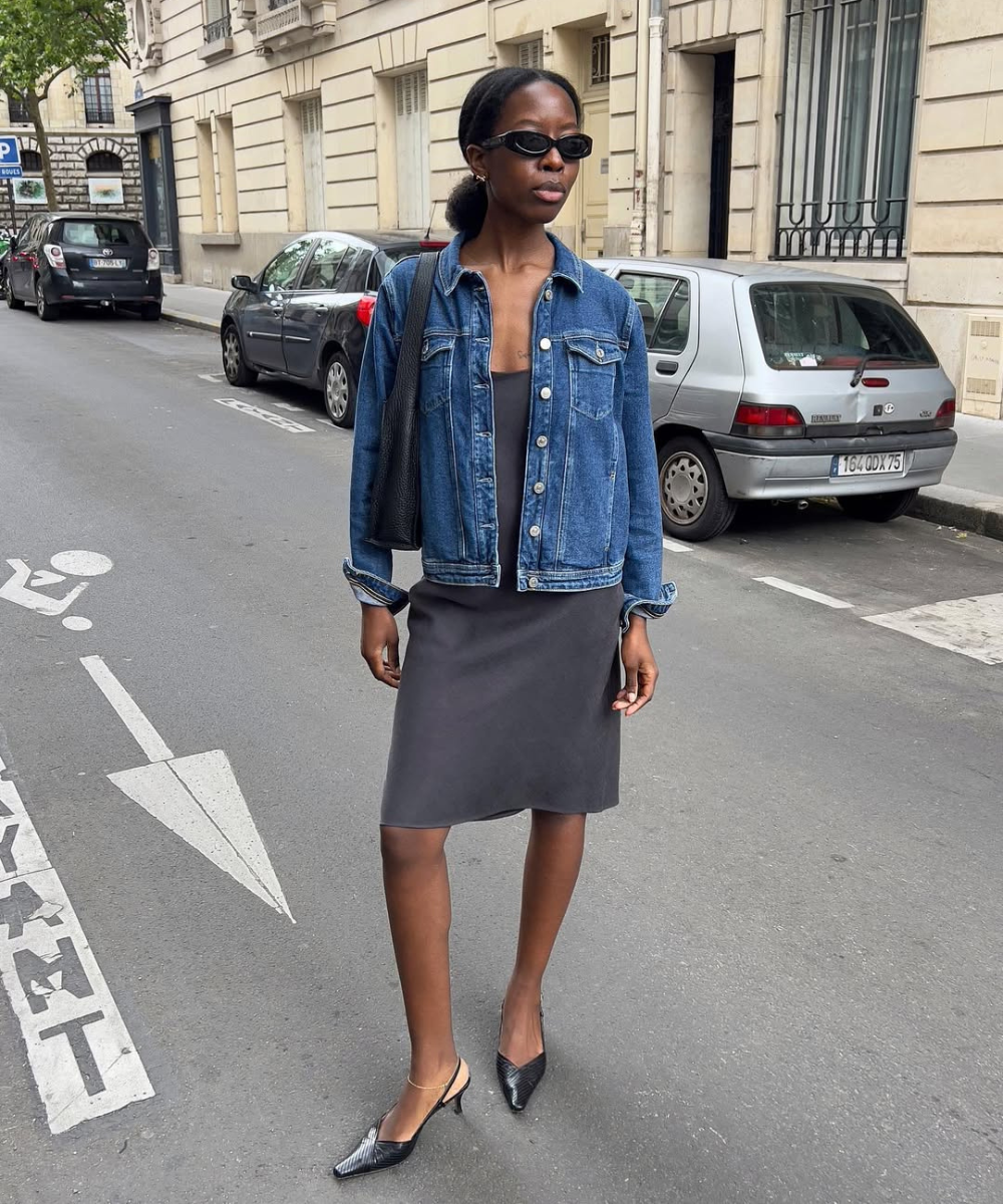Looks com scarpin: modelo posa na rua com jaqueta jeans, vestido cinza reto e slingback preto, em clima urbano elegante.