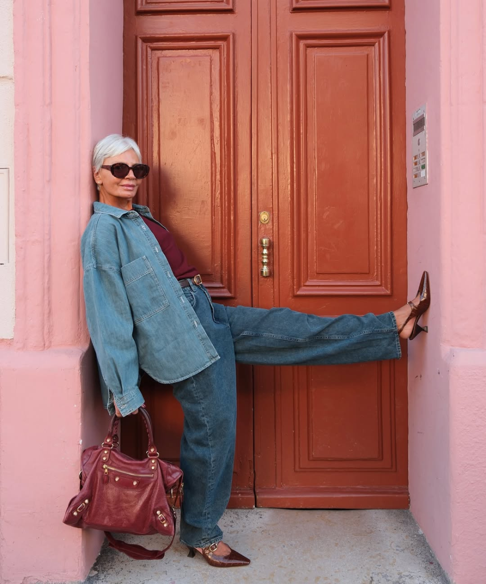 Looks com scarpin: modelo posa de jeans amplo, camisa oversized e bolsa vinho diante de porta rosada, com atitude elegante.