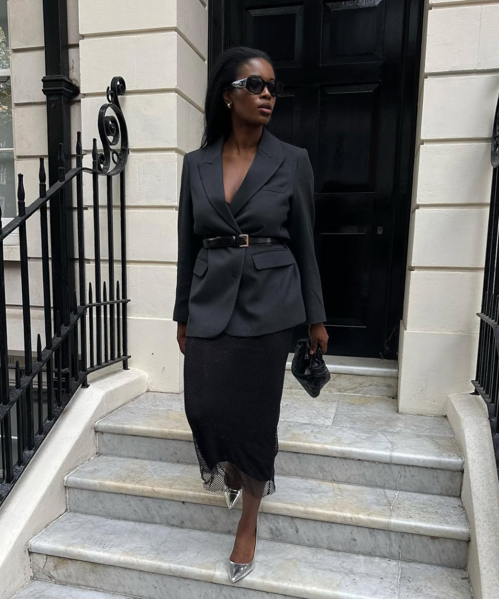 Looks com scarpin: modelo posa em blazer acinturado preto, saia midi texturizada e scarpin prata, com elegância urbana.