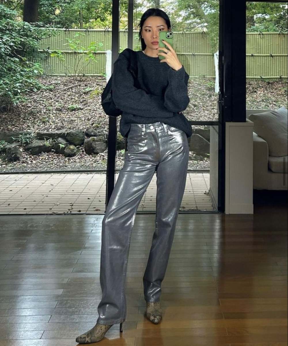 Modelo posa com calça resinada prata de brilho intenso, tricô preto amplo e ankle boot animal print em clima sofisticado.